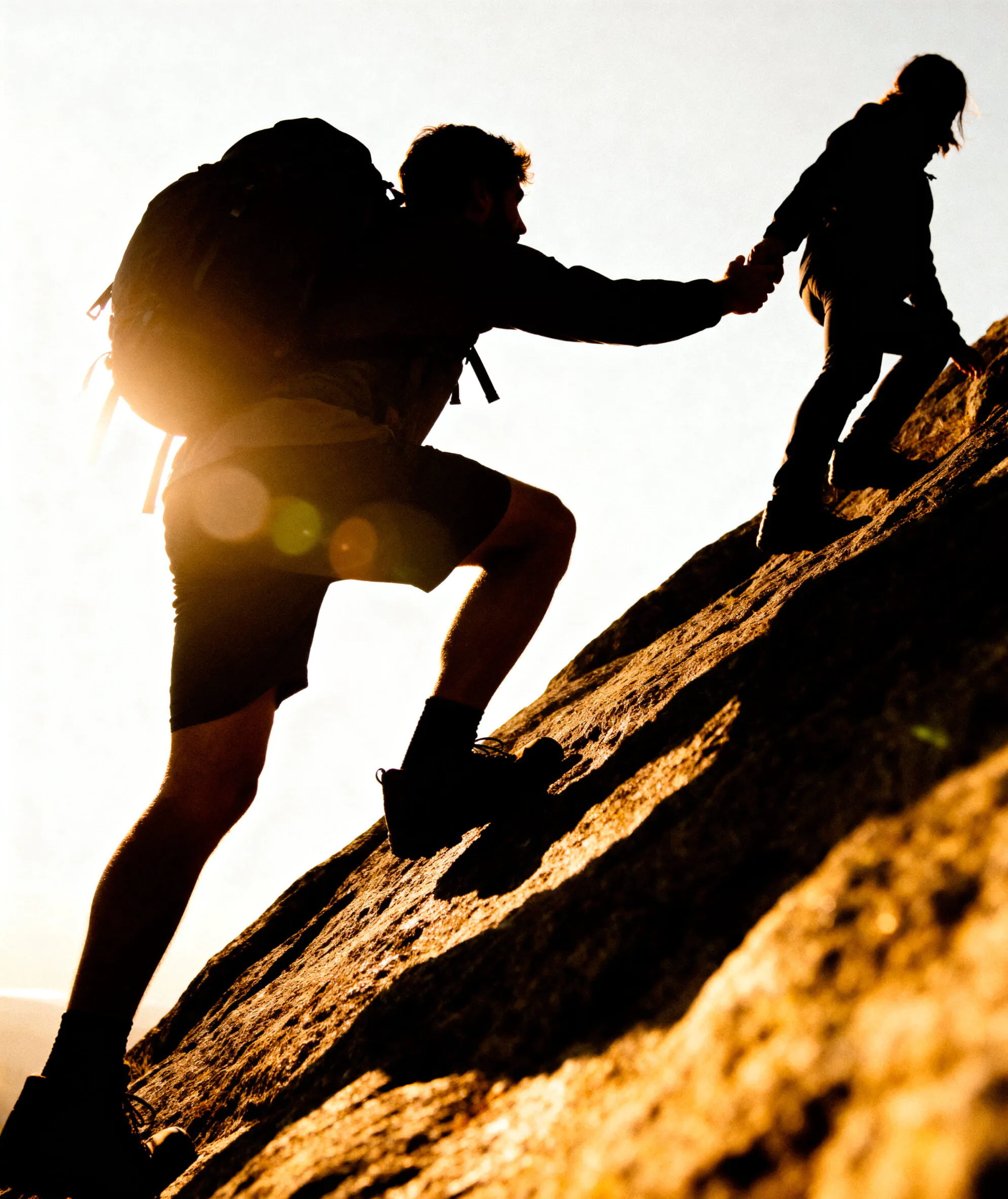 Two climbers ascending a rocky slope during sunset, showcasing teamwork and adventure in nature.